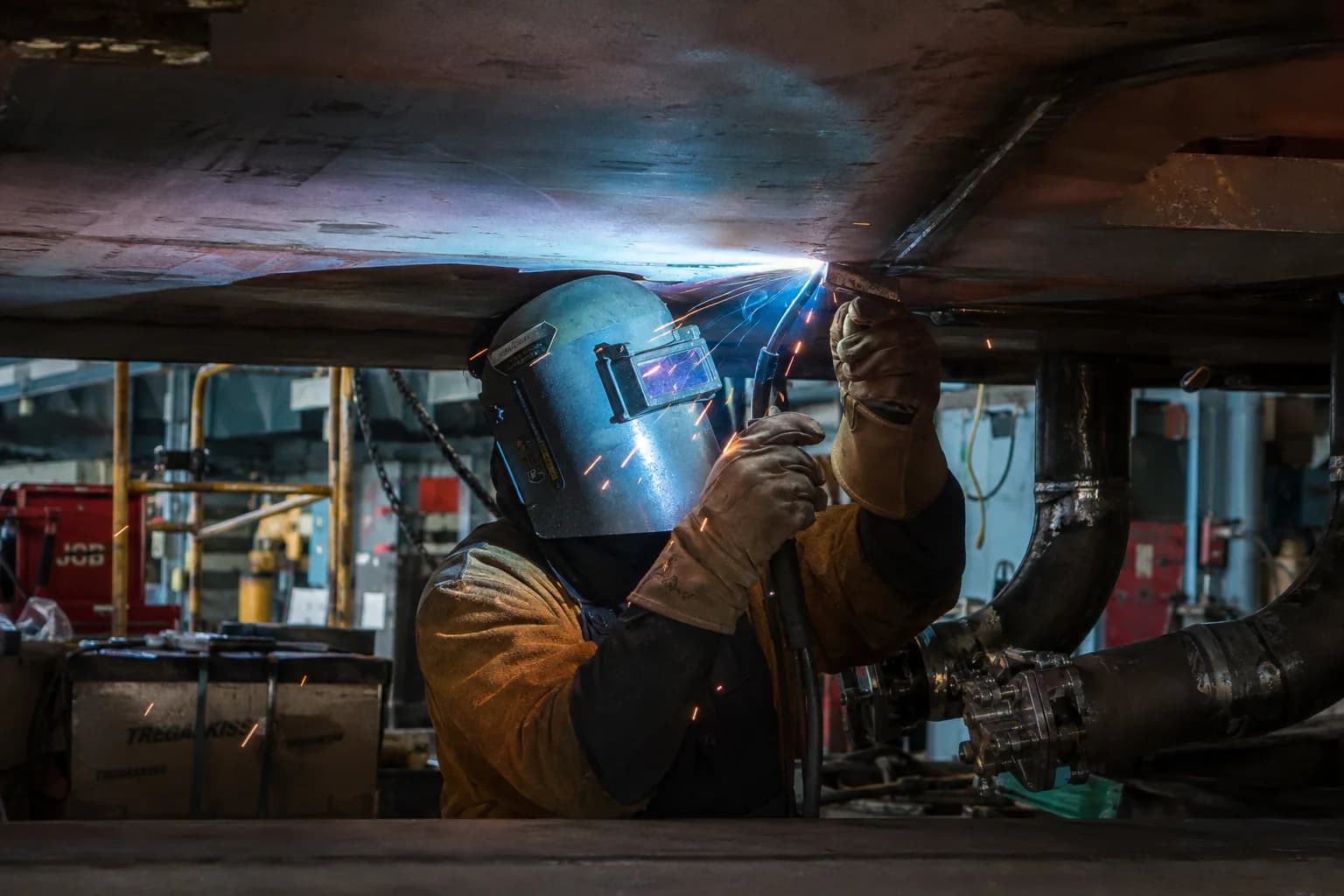 Welder working overhead on structural steel, sparks falling